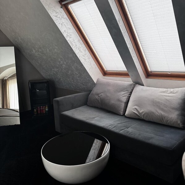 A modern loft bedroom with a sloped ceiling, a grey sofa, a round coffee table, and skylights. - Agusta Spa Hotel (Veliko Tarnovo)