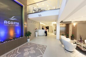 A hotel reception area with a modern design, including a reception desk, seating area, and a decorative wall with a logo. - Agusta Spa Hotel (Veliko Tarnovo)