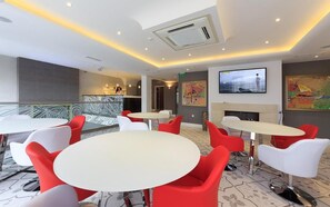 A modern hotel lobby with round tables and red chairs, a reception desk, and artwork on the walls. - Agusta Spa Hotel (Veliko Tarnovo)