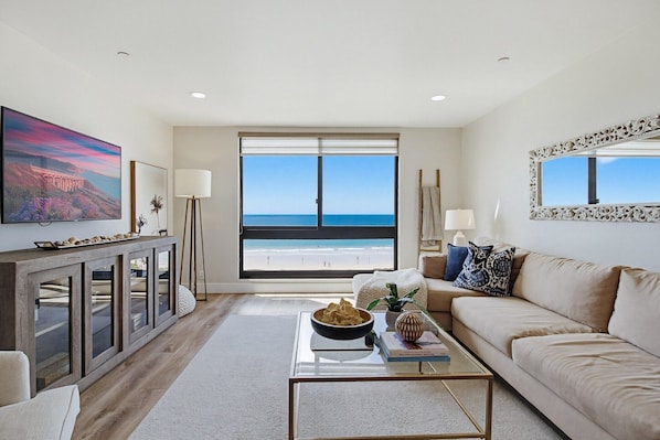 A living room with a large window, a sofa, a coffee table, and a TV on a stand. - Sparkling sunset views of PACIFIC BEACH!! (San Diego)