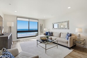 A modern living room with a large window, a sofa, a coffee table, and a side table. - Sparkling sunset views of PACIFIC BEACH!! (San Diego)