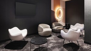 Uma área de estar moderna com cadeiras brancas, uma mesa redonda e um lustre fixado na parede.