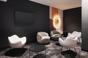 A modern lounge area with white chairs, a round table, and a wall-mounted light fixture. - The Hotel Katowice (Katowice)