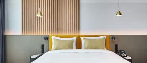 A modern hotel room with a large bed, two bedside tables, a wall-mounted phone, and two pendant lights.