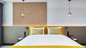 Quarto de hotel com cama, duas mesinhas de cabeceira, telefone fixado na parede e duas luminárias pendentes.