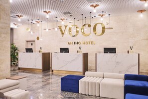 Un espace d’accueil d’hôtel doté de comptoirs en marbre, d’un bureau d’accueil et d’un coin salon avec des canapés.