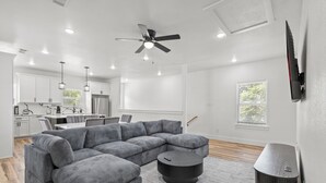 A modern living room with a sectional sofa, a round coffee table, a TV on the wall, and a ceiling fan. - Modern Fort Worth Stay w/ EV Charger Near TCU, ATT Stadium & Downtown (Fort Worth)