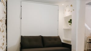 Een kamer met een donkerbruine bank, een witte kledingkast en een kleine plant op een plank.