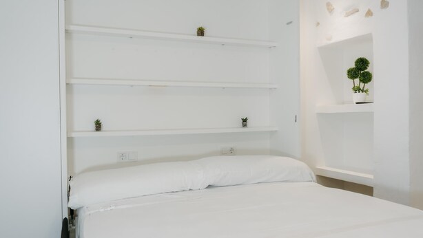 Een slaapkamer met een bed, witte muren en meerdere planken met kleine planten.