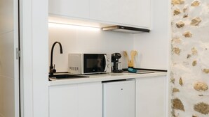 Een kleine keuken met witte kastjes, een magnetron, een koffiezetapparaat en een vaatwasser.