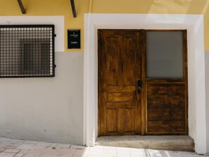 Une porte en bois avec un panneau de verre, un portail en métal et une enseigne indiquant « COURBU » sur un mur jaune.