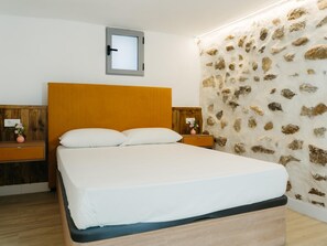 A bedroom with a wooden headboard, a single bed with white bedding, a nightstand with a vase, and a stone-patterned wall. - Courbu Harbor's Light (La Vila Joiosa)