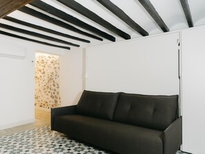 Une pièce avec un canapé foncé, un tapis à motifs, une armoire blanche et un mur en pierre.