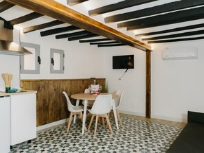 A modern kitchen with a dining area, wooden ceiling beams, a TV, and a patterned floor. - Courbu Harbor's Light (La Vila Joiosa)
