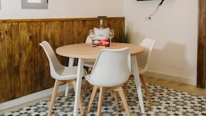 Zona pranzo con tavolo rotondo, sedie bianche, una bottiglia di vino e un televisore montato a parete.