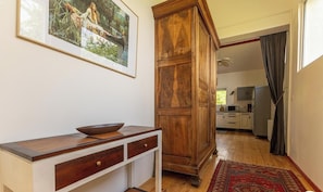 A hallway with a wooden cabinet, a white console table with a bowl, a framed picture on the wall, and a view into a kitchen area. - Les Amandiers - CEYRAT (CEYRAT)