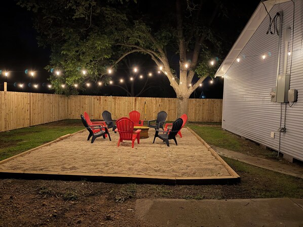 A backyard with a wooden fence, a tree, and a patio with chairs and a table.