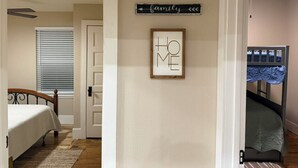 Une chambre avec un lit superposé, un panneau encadré accroché au mur et une porte donnant sur une autre pièce.