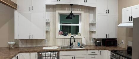 A kitchen with white cabinets, a stainless steel sink, a microwave, and an oven.