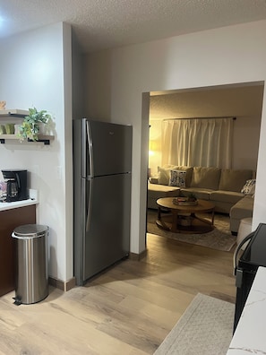 A modern kitchen with a stainless steel refrigerator, a coffee maker, and a trash bin.