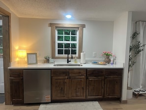A kitchen with a built-in dishwasher, wooden cabinets, a window with a view, and a countertop with a lamp and a framed welcome sign.
