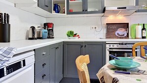 Una cocina compacta con horno integrado, cafetera y comedor con mesa lista para dos.