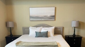 A neatly made bed with a headboard, two bedside tables, and a wall-mounted painting. - Mountain Views, Air Force Academy, Hot Tub, Pet Friendly, Hiking, Trails, Dining (Colorado Springs)
