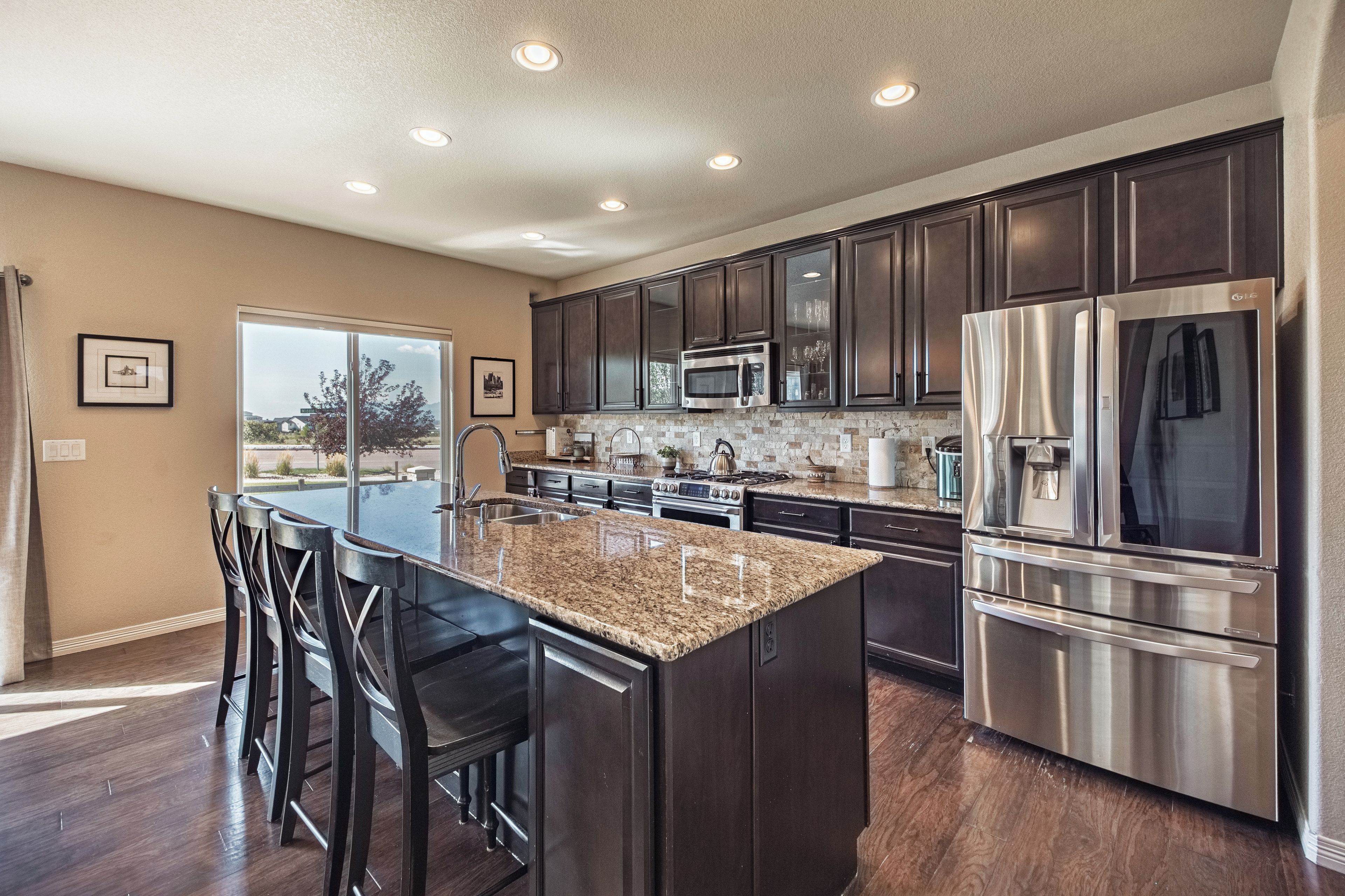 A modern kitchen with dark cabinets, stainless steel appliances, and a large island with bar stools.