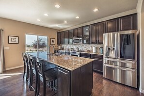 A modern kitchen with dark cabinets, stainless steel appliances, and a large island with bar stools. - Mountain Views, Air Force Academy, Hot Tub, Pet Friendly, Hiking, Trails, Dining (Colorado Springs)