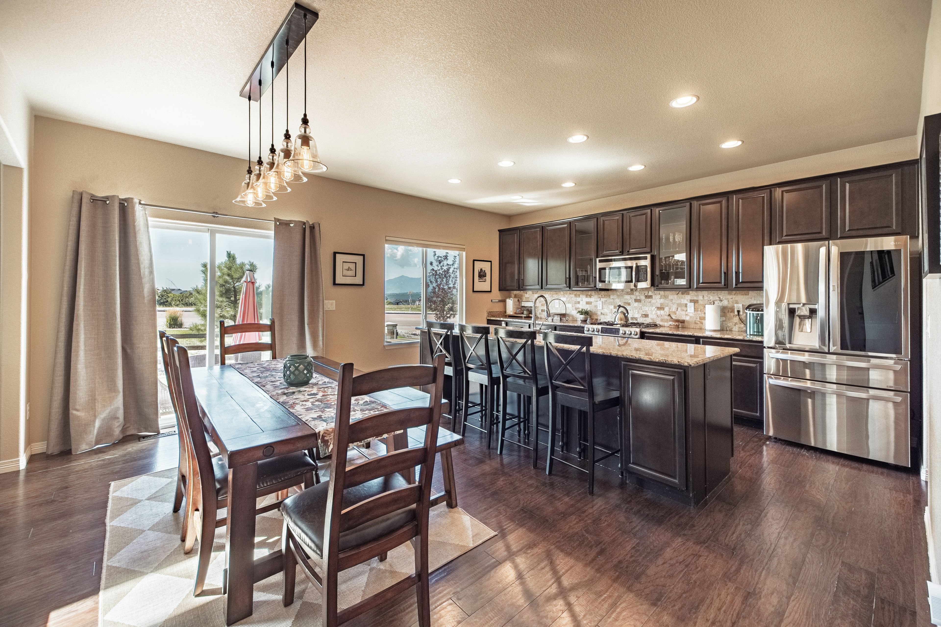 A modern kitchen with dark wood cabinets, stainless steel appliances, and a dining area with a wooden table and chairs.