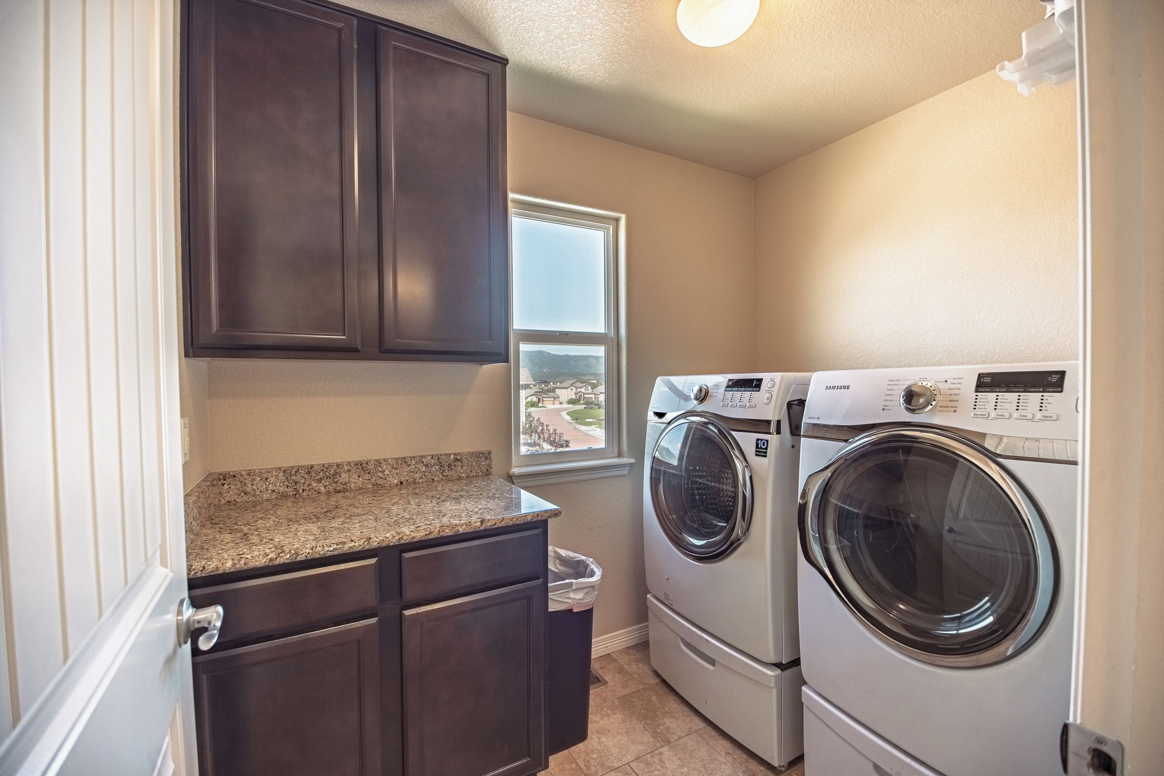 A laundry room with dark cabinets, a granite countertop, and a front-loading washer and dryer.