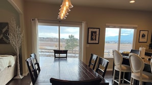 Comedor con mesa y sillas de madera, ventanas amplias con vistas y una araña.