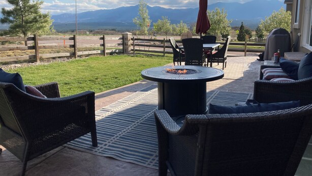 Un patio al aire libre con mobiliario de mimbre, una mesa redonda con una chimenea y vistas a montañas.