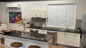 A modern kitchen with a central island, white cabinets, a stainless steel sink, and a large window with blinds.