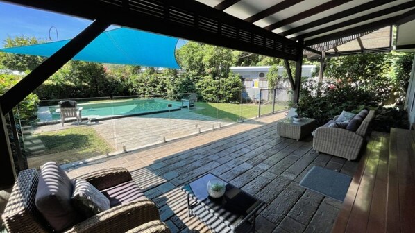 A covered outdoor patio with wicker furniture, a pool, and a view of the backyard.