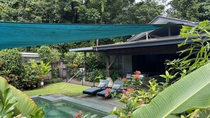 A backyard with a pool, lounge chairs, and a covered patio area.