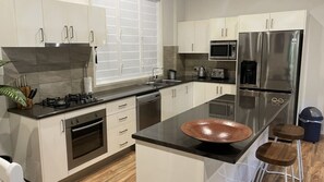 A modern kitchen with white cabinets, stainless steel appliances, a black countertop, and a copper bowl centerpiece.