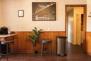 A kitchen with wooden paneling, a coffee machine, two stools, a trash can, and a potted plant. - 5 Bedroom Mid Term Rental in Bryan "The WHOOP" (Bryan)