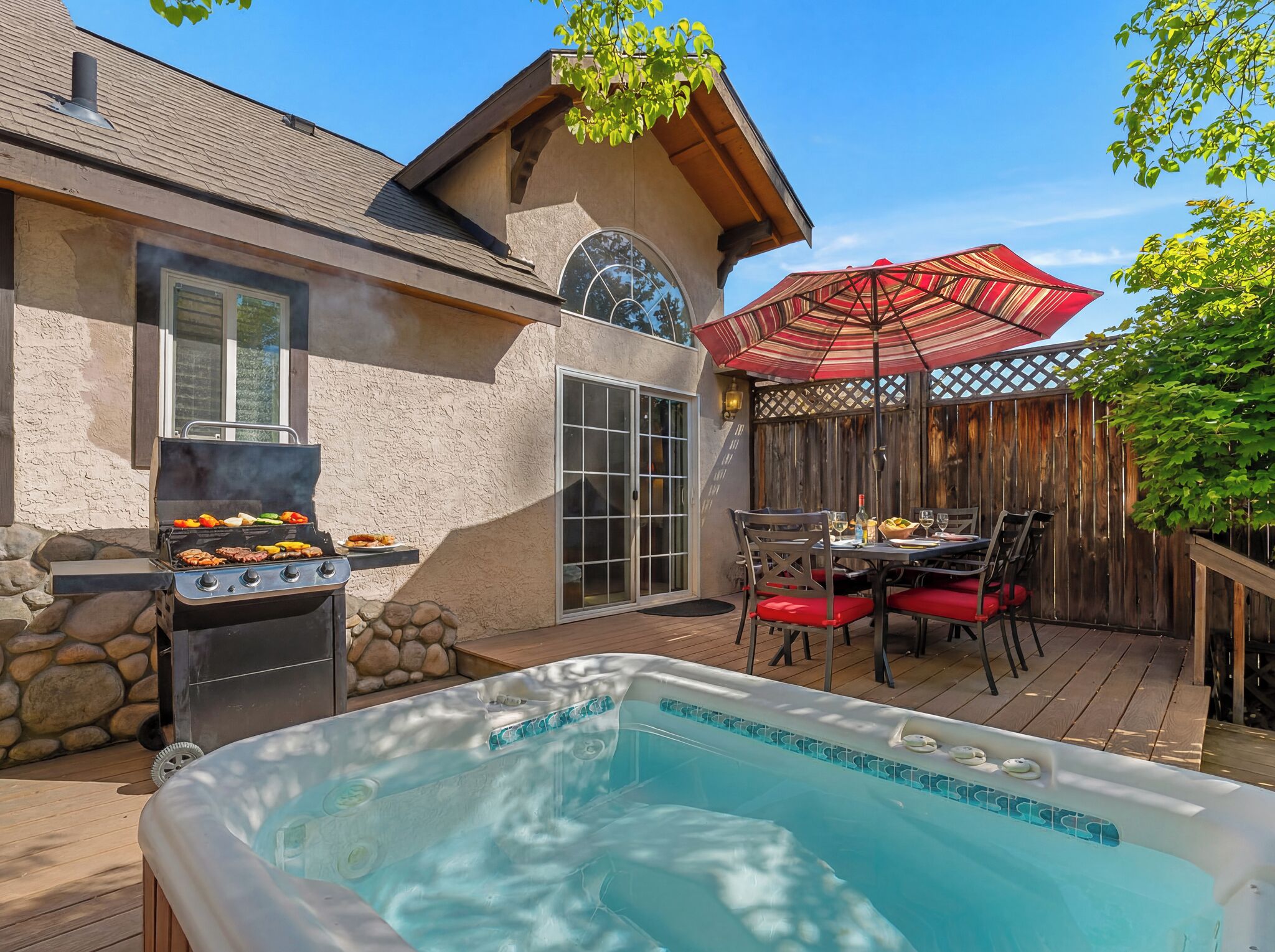 A backyard with a hot tub, a barbecue grill, and a dining area with outdoor furniture.