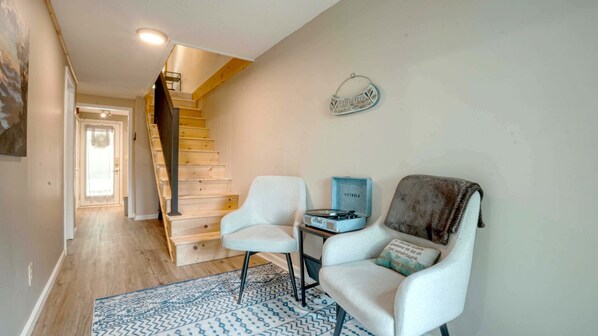A staircase with wooden steps and a handrail, a white armchair, a small table with a record player, and a wall-mounted decorative item.