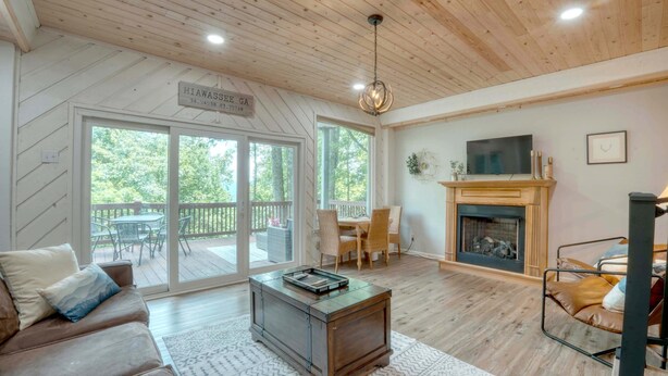 A spacious living room with a fireplace, a dining area with outdoor seating, and a large sliding glass door leading to a deck. - Summit View - Mountain Top View & Gas Fireplace (Hiawassee)