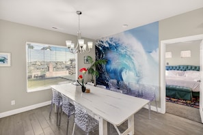 A dining area with a white table, clear chairs, a chandelier, and a large wave mural on the wall. - Grand Group Rental,19BR Luxury Compound -Sleeps 54 (Hurricane)
