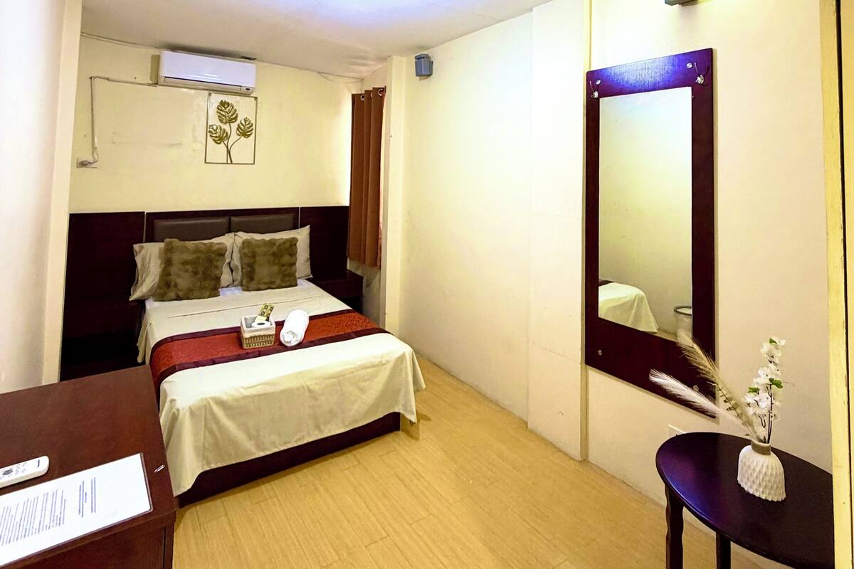 Una habitación de hotel con cama, mesita de noche, espejo y un pequeño escritorio con silla.