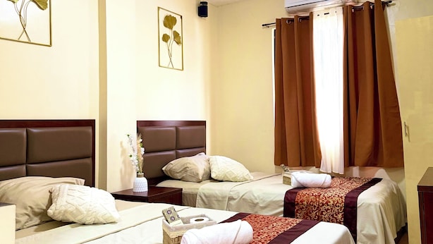 Habitación de hotel con dos camas, ventilador de techo, equipo de aire acondicionado y una ventana con cortinas.