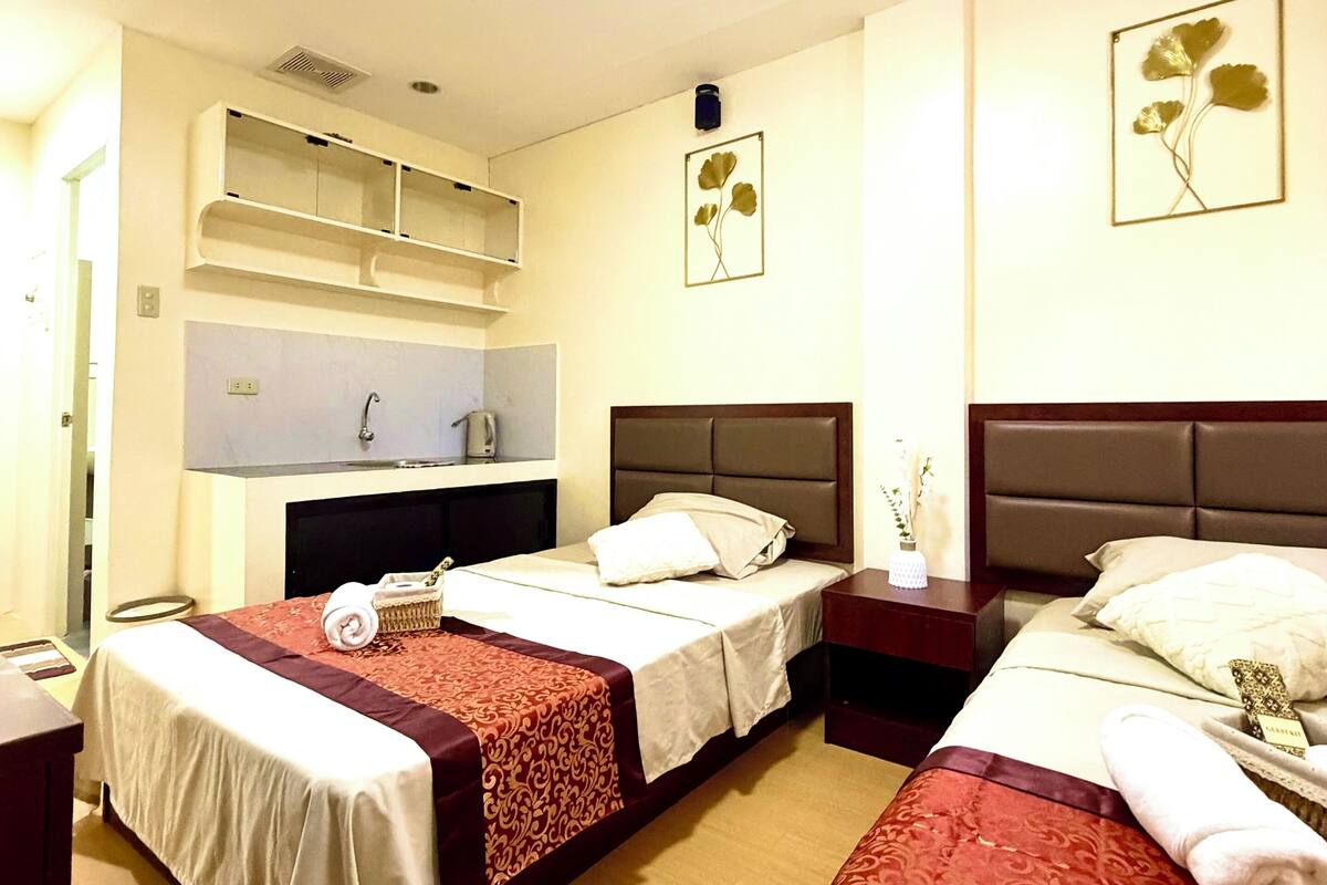 Una habitación de hotel con tres camas, un pequeño espacio kitchenette y un baño.
