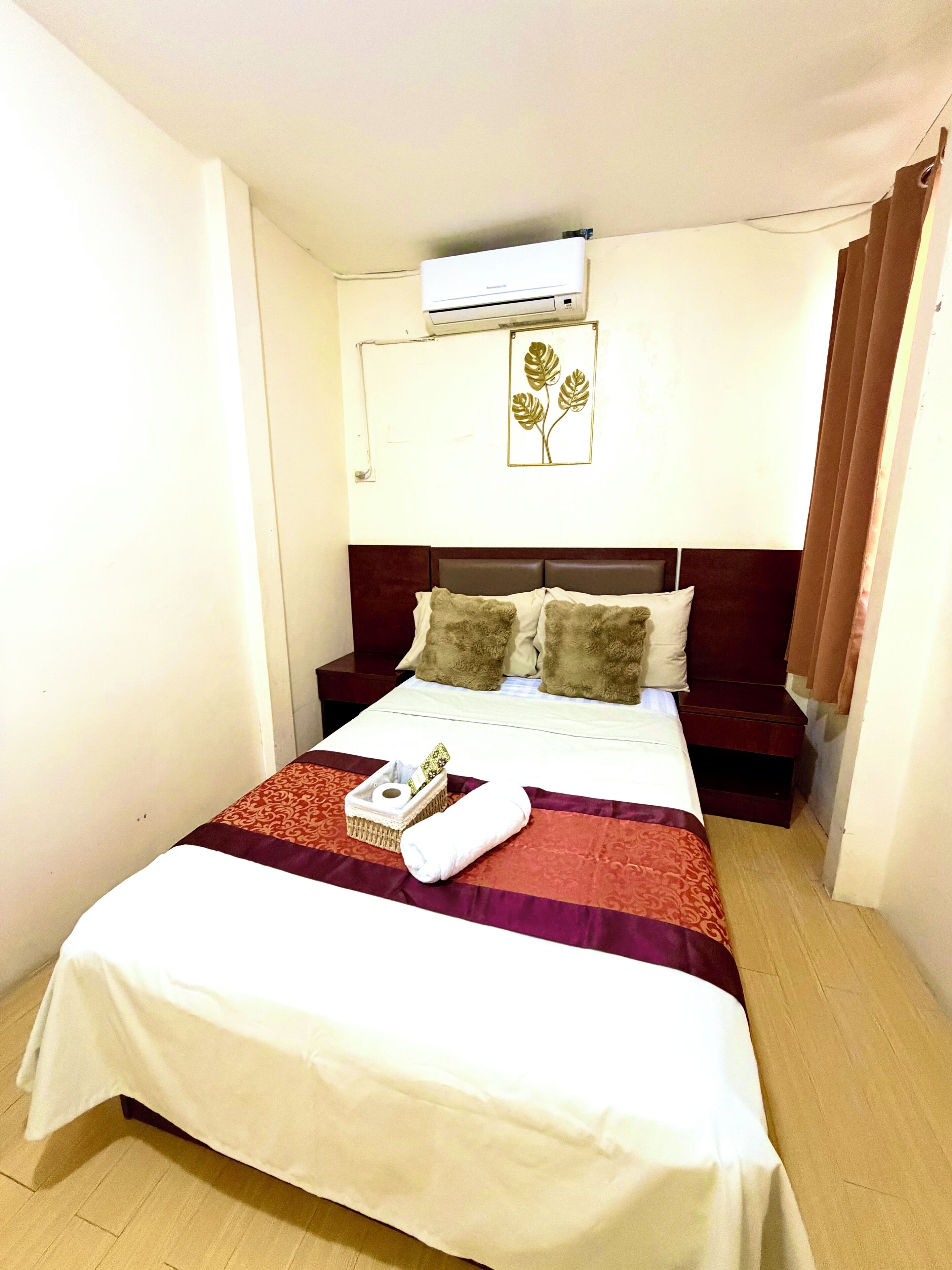 A hotel room with a bed, a bedside table, a wall-mounted air conditioner, and a framed artwork.