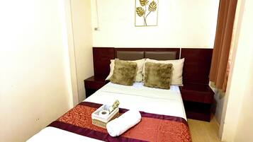 A hotel room with a bed, a bedside table, a wall-mounted air conditioner, and a framed artwork.