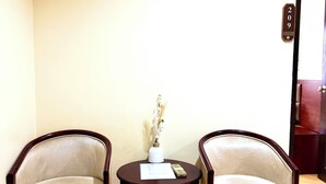 Una habitación con dos sillones, una mesita redonda y suelo de madera. Se observa una puerta con el símbolo de número.