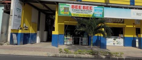 A commercial building with a yellow and blue facade, a sign for 'BEE BEE CONSTRUCTION,' and a palm tree in front.