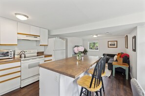 A compact kitchen with white cabinets, a built-in oven, and a small dining area with a wooden table and chairs. - Spring Haven Lakeside Casita | Quick Trip Downtown (Seattle)